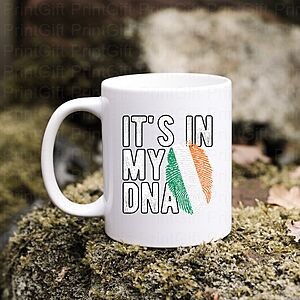 White mug on a mossy rock with the text "IT'S IN MY DNA" printed alongside a DNA double helix in the colors of the Irish flag: green, white, and orange.