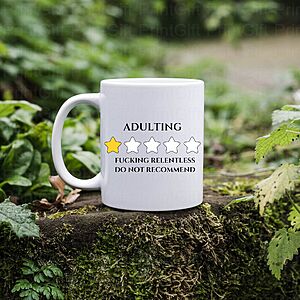 White mug on a mossy log, surrounded by greenery. It has a rating system with one gold star and four empty stars. Text reads, "Adulting: F*cking relentless do not recommend.