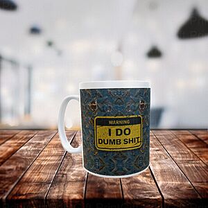 A coffee mug sits on a wooden table in a blurred indoor setting. The mug displays a humorous sign with the text "WARNING: I DO DUMB SHIT" against a patterned background.